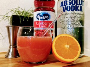 Afbeelding van tumbler glas met cocktail, sinaasappel, een fles cranberrysap en een fles wodka