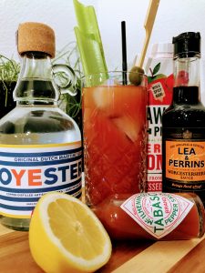 Afbeelding van een glas bloody mary met garneringen, flesje tabasco, citroen, fles worcester sauce, een pak tomatensap en een fles wodka